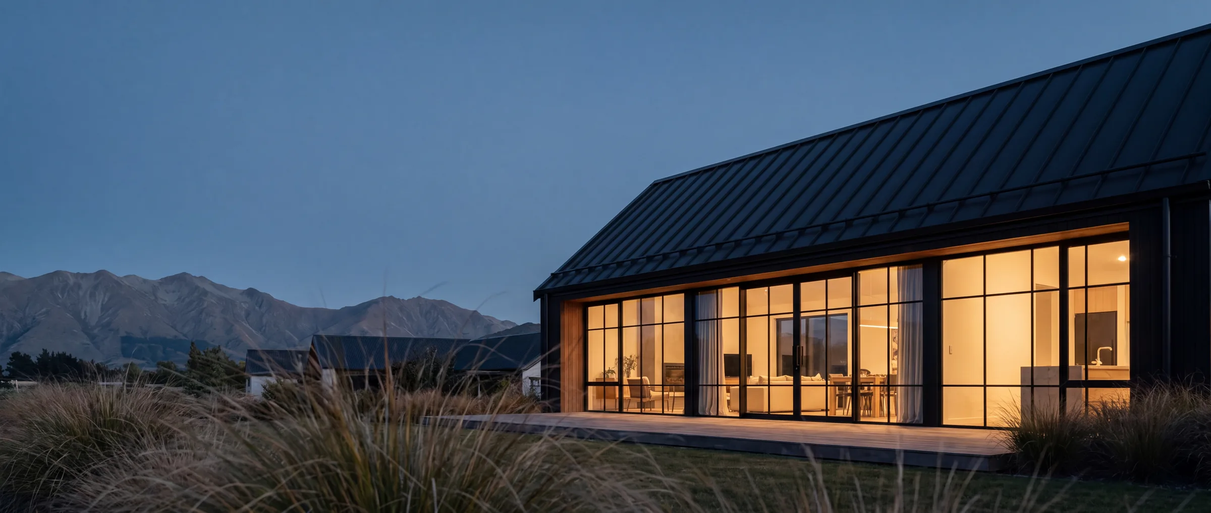 Готовый barn house с террасой и тёплым светом внутри на фоне гор